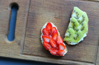 Bruschetta süzme peynir ve taze çilek ve kivi çilek tost kepekli ekmek ile. Yumuşak peynirli fransız tostu. Yaz pikniği zamanı, ahşap rustik arka planda vejetaryen sandviçler. Kopya alanı. Sağlıklı beslenme kavramı.
