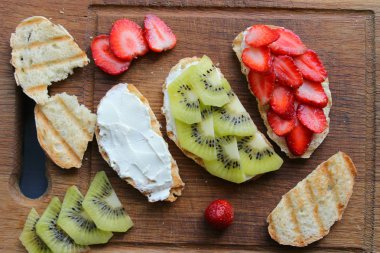 Bruschetta süzme peynir ve taze çilek ve kivi çilek tost kepekli ekmek ile. Yumuşak peynirli fransız tostu. Yaz pikniği zamanı, ahşap rustik arka planda vejetaryen sandviçler. Kopya alanı. Sağlıklı beslenme kavramı.
