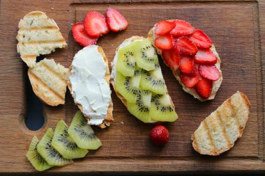 Bruschetta süzme peynir ve taze çilek ve kivi çilek tost kepekli ekmek ile. Yumuşak peynirli fransız tostu. Yaz pikniği zamanı, ahşap rustik arka planda vejetaryen sandviçler. Kopya alanı. Sağlıklı beslenme kavramı.