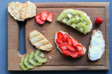 Bruschetta süzme peynir ve taze çilek ve kivi çilek tost kepekli ekmek ile. Yumuşak peynirli fransız tostu. Yaz pikniği zamanı, ahşap rustik arka planda vejetaryen sandviçler. Kopya alanı. Sağlıklı beslenme kavramı.