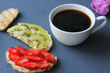 Kahvaltı çok güzel. Bir fincan kahve ve bruschetta süzme peynir ve taze çilek ve kivi çilek kızarmış bütün tahıl ekmek. Yumuşak peynir ile Fransız tost. Yaz piknik zamanı, ahşap rustik arka planda vejetaryen sandviçler. 