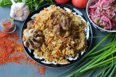 Pilav et ve baharat tabağının üzerinde.tahta bir arka plan üzerinde bir tabakta pilav, üst görünümü. Doğu mutfağı kavramı. Ev yapımı Özbek kuzu pilavı dökme demir tencerede servis edilir. Kopya alanı. Oryantal ornamen ile bir tabakta pilav ve malzemeler