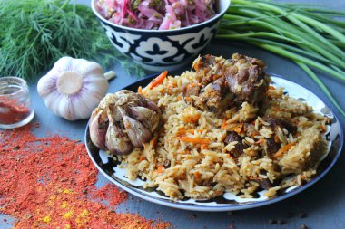 Pilav et ve baharat tabağının üzerinde.tahta bir arka plan üzerinde bir tabakta pilav, üst görünümü. Doğu mutfağı kavramı. Ev yapımı Özbek kuzu pilavı dökme demir tencerede servis edilir. Kopya alanı. Oryantal ornamen ile bir tabakta pilav ve malzemeler