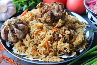 Pilav et ve baharat tabağının üzerinde.tahta bir arka plan üzerinde bir tabakta pilav, üst görünümü. Doğu mutfağı kavramı. Ev yapımı Özbek kuzu pilavı dökme demir tencerede servis edilir. Kopya alanı. Oryantal ornamen ile bir tabakta pilav ve malzemeler