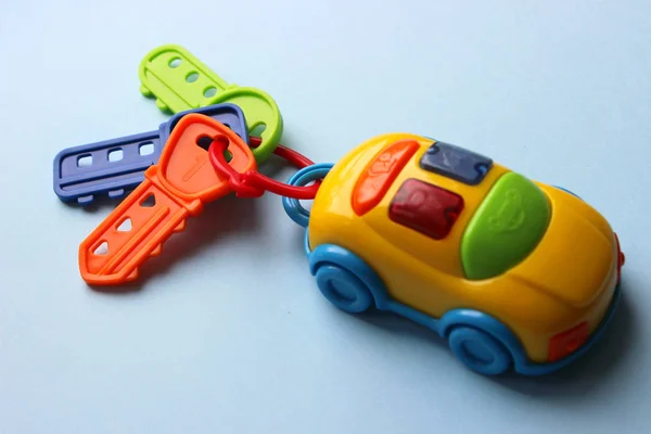 Children\'s toy car with keys. Toy keychain from the car. Multi-colored key with keychain. The hook from the toy car is isolated on a blue background.