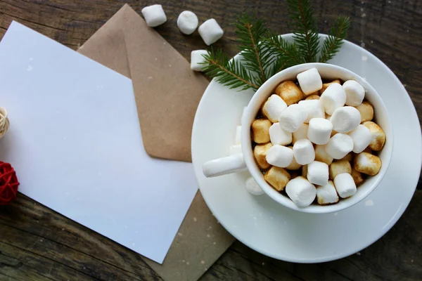 Cup with homemade Christmas hot chocolate drink, marshmallows and holiday greeting card on wooden background. — Stock Photo, Image