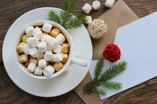 Cup with homemade Christmas hot chocolate drink, marshmallows and holiday greeting card on wooden background. — Stock Photo, Image