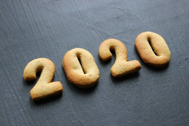 2020 yeni yıl geçmişi. Fırınlanmış mektuplar Mutlu yıllar ve 2020 numaralar, yıldızlar, siyah bir arka planda kar taneleri. Zencefilli tebrik kartı. Tahta siyah bir masada zencefilli çörekten yılbaşı kartı. Kavram 2020