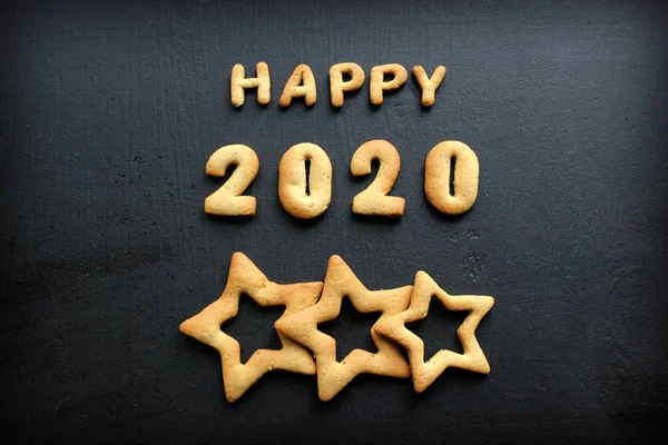 2020 yeni yıl geçmişi. Fırınlanmış mektuplar Mutlu yıllar ve 2020 numaralar, yıldızlar, siyah bir arka planda kar taneleri. Zencefilli tebrik kartı. Tahta siyah bir masada zencefilli çörekten yılbaşı kartı. Kavram 2020