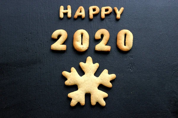 2020 yeni yıl geçmişi. Fırınlanmış mektuplar Mutlu yıllar ve 2020 numaralar, yıldızlar, siyah bir arka planda kar taneleri. Zencefilli tebrik kartı. Tahta siyah bir masada zencefilli çörekten yılbaşı kartı. Kavram 2020
