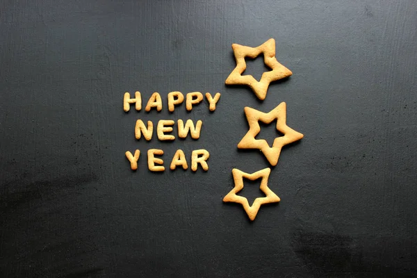 Baked letters Happy New year, stars, snowflakes on a black background.Greeting card with gingerbread. Card with New year from gingerbread on a wooden black table. Text happy New year from ginger cookies on a baking sheet