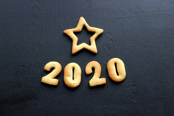 2020 yeni yıl geçmişi. Fırınlanmış mektuplar Mutlu yıllar ve 2020 numaralar, yıldızlar, siyah bir arka planda kar taneleri. Zencefilli tebrik kartı. Tahta siyah bir masada zencefilli çörekten yılbaşı kartı. Kavram 2020