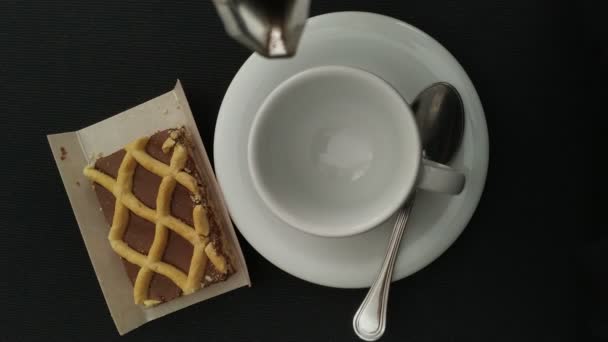 エスプレッソカップに間欠泉コーヒーメーカーからブラックコーヒーを注ぐトップビュー チョコレートケーキの一部 ミニマリストの背景 フラットレイスタイル — ストック動画