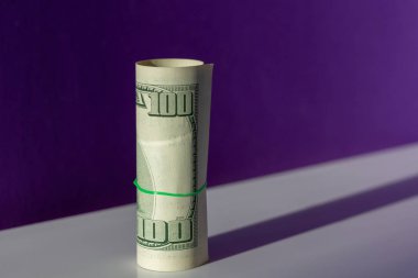 Yüz dolar, bir saman bükülmüş mor bir arka plan üzerinde beyaz bir tablo üzerinde durmak. İş kavramı boşluk ile moda renklerde. Para açık ve göz alıcı fotoğraf.