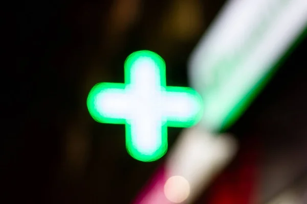 Green signboard of a pharmacy with bright neon lights at night. Blurred photo with defocus. Neon advertising pharmacy at night.