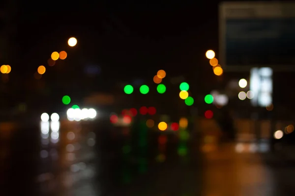 Lanterns of the night city illuminate the road. Blurred photo with defocus. Headlights of cars in the night city. Multicolored bright festive night lights bokeh.