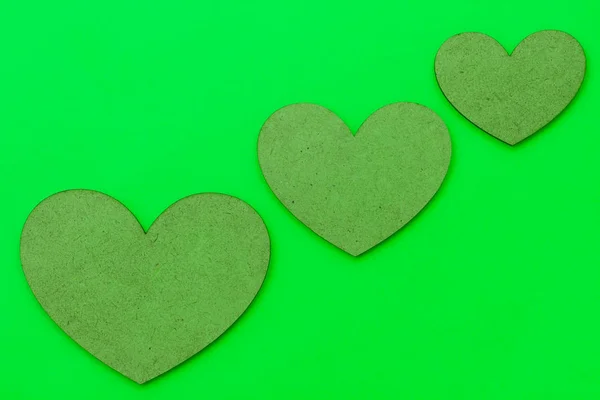 Three hearts of different sizes of brown color on a green background. Concept on the theme of love for Valentine\'s Day.