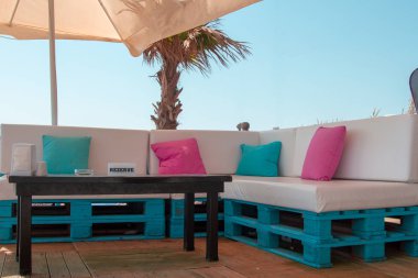 Kanepeler euro palet ve parlak yumuşak yastık ile ayrılmış beach tablo. Plaj şemsiyesi altında ayrılmış bir tablo. Euro palet yeşil ve pembe yastıkları ile büyük deri koltuklar. Beach tarzı.