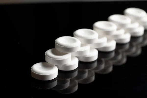 Three rows of white pills close-up on a black background with a mirror reflection. Rows of white pills go away with a perspective. Abstract minimalistic black concept. Same white pills.