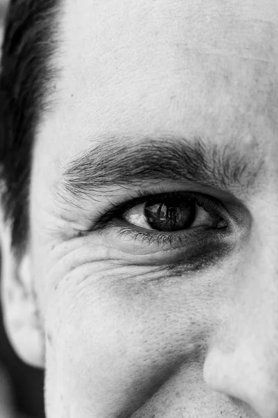 Fragment of a man\'s face: right eye and nose to compile an identikit. Fragment of the wrinkled face of a young guy. Smiling eye of a man. Black and white photo.