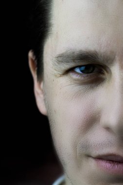 Şu kendinden emin bir adamın yüzünü yarısı kapatın. Siyah bir arka plan üzerinde bir erkek yüz yakın çekim parçası. Bir erkek yüz cilt dokusunu, kırışmış gözler ile Studio fotoğraf.