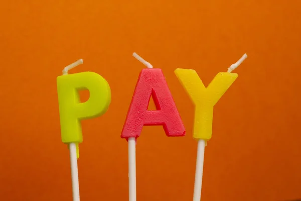 Concept word Pay from festive multi-colored wax paraffin candles on orange background.