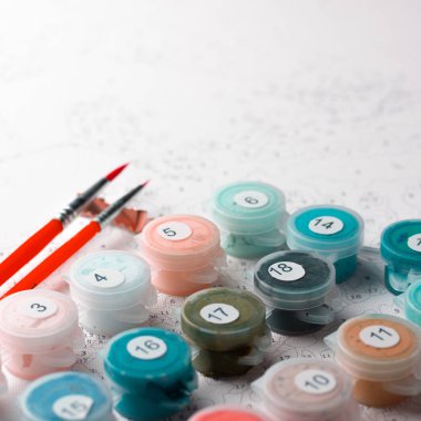 Kapları numaralarına göre ev resim boyaları ile kümesi. Hobi resim tuval ile akrilik rakamlarla boyar. Boya fırçaları ve renkli boyalar. Kırmızı fırçalar ile. Kare fotoğraf.