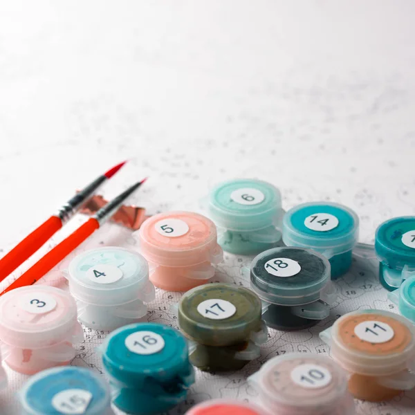 Kapları numaralarına göre ev resim boyaları ile kümesi. Hobi resim tuval ile akrilik rakamlarla boyar. Boya fırçaları ve renkli boyalar. Kırmızı fırçalar ile. Kare fotoğraf.