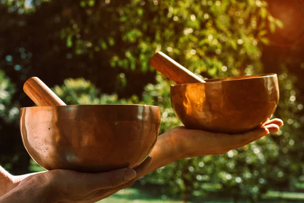 Two bronze singing bowls in female hands with wooden sticks to e