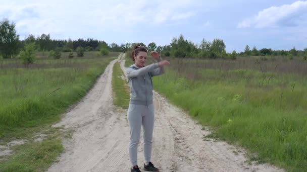 A young sports female does a warm-up in the fresh air in the middle of a dirt road outside the city. Slow-motion. — Stock Video