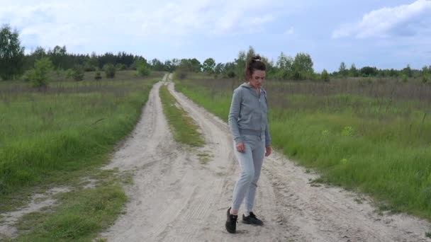 A young pretty sports Female kneads her ankles, knees and pelvic joints in the fresh air in the middle of a dirt road outside the city. Slow-motion. — Stock Video