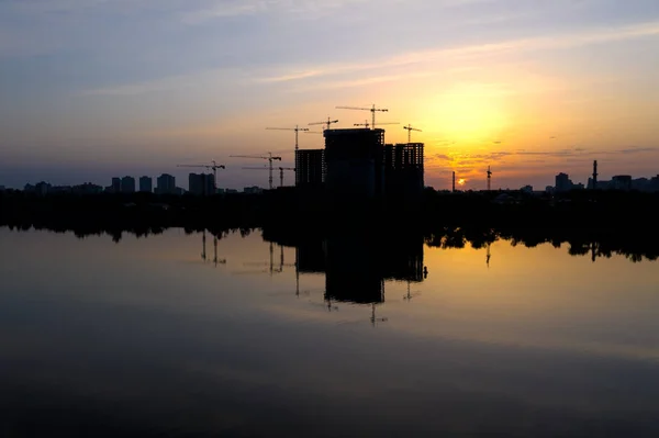 Beautiful urban construction site silhouettes at Dawn. Morning Cityscape with Reflection in water.