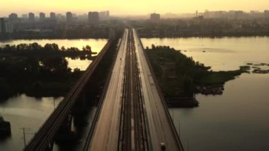 Şafak vakti ender bulunan arabalarla dolu uzun bir köprünün üzerinden geçen sinematik bir insansız hava aracı. Nehrin üzerindeki köprüden drone uçuşu. Doğan güneşin ışınlarıyla ada..