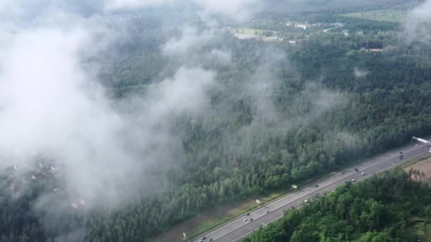 Nízké ranní mraky nad velkou dálnicí vedoucí lesem. Filmový průlet dronem skrz mraky.. — Stock video