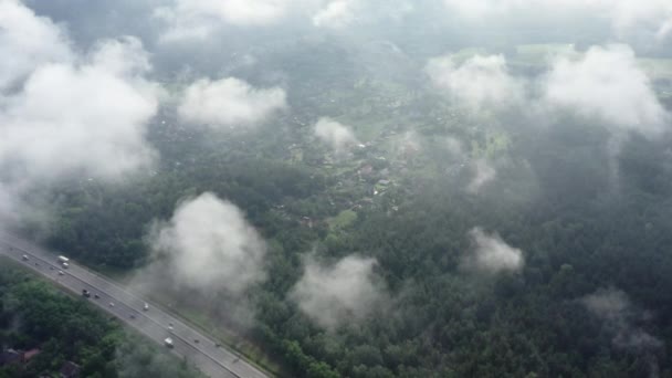 Vlucht ver Lage ochtend pluizige wolken over een grote snelweg die door het bos. Een filmische flyby van een drone door de wolken. — Stockvideo