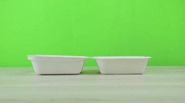 Yeşil arka plandaki bir karton kutuyu kapatmak. Bir adam yeşil arka planda tek kullanımlık bir eko yiyecek konteynırını kapatıyor..