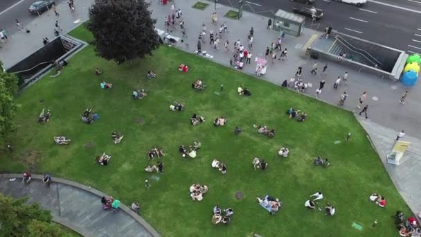 Les couples amoureux et d'autres personnes se reposent sur la pelouse verte à la fin de la journée. Vue Aérienne. Zone verte de loisirs dans la ville. Les gens se reposent sur une pelouse verte dans le centre de Kiev. — Video