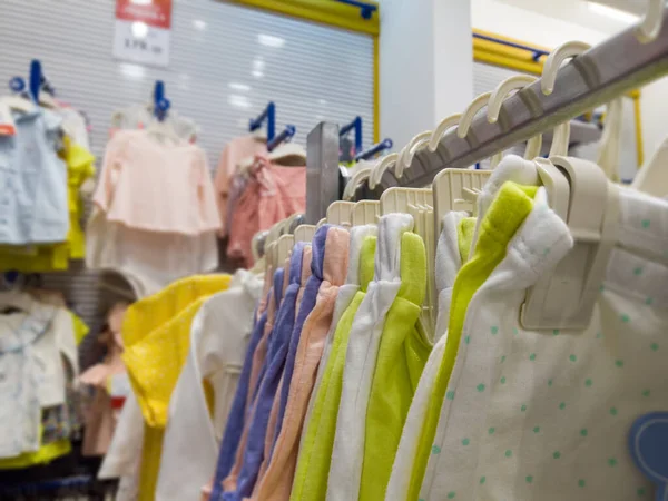 A collection of multi-brand childrens clothing of bright colors hangs on hangers in the clothing store, selective focus