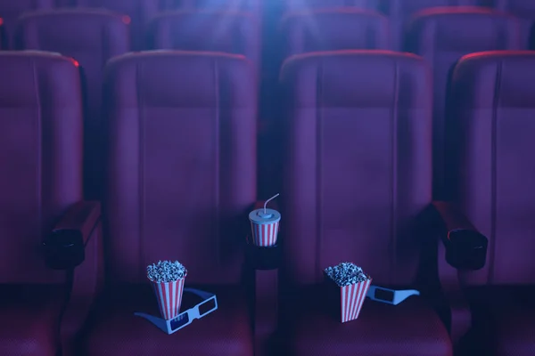 Cine película concpet con palomitas de maíz, vasos 3d, palomitas de maíz y taza con una bebida. Concepto de cine con luz azul. Sillas rojas en la sala de cine. Ilustración 3D — Foto de Stock