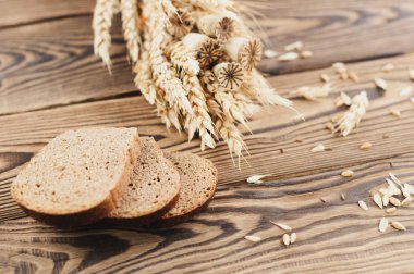 Buğday ve haşhaş bir demet ve dağınık tahıl ve eski rustik ahşap kalas üzerinde ekmek üç dilim çok