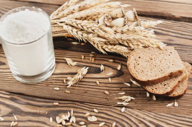 Buğday ve haşhaş bir demet ve dağınık tahıl ve eski rustik ahşap kalas üzerinde cam ekmek ve un üç dilim çok