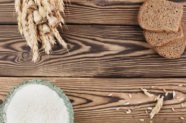 Eski rustik ahşap kalaslar üzerinde cam kase buğday ve haşhaş ve dağınık tahıl ve ekmek ve un üç dilim bir demet