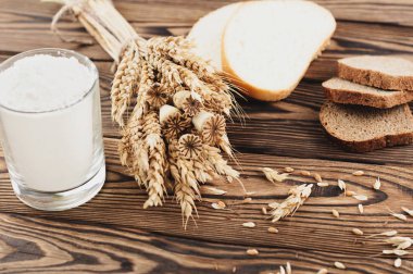 Buğday ve haşhaş bir demet ve dağınık tahıl ve ekmek ve un dilimleri eski rustik ahşap plakalar üzerinde cam bir demet