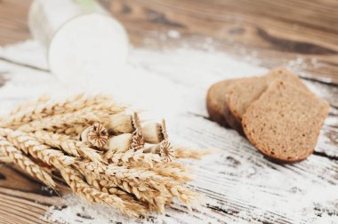 Eski rustik ahşap kalaslar üzerinde cam ve ekmek dilimleri dökülen buğday ve haşhaş ve un bir demet