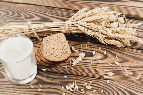 Buğday ve haşhaş bir demet ve dağınık tahıl ve eski rustik ahşap kalas üzerinde cam ekmek ve un üç dilim çok