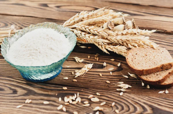 Eski rustik ahşap kalaslar üzerinde cam kase buğday ve haşhaş ve dağınık tahıl ve ekmek ve un üç dilim bir demet