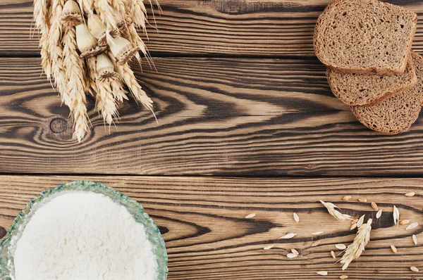 Eski rustik ahşap kalaslar üzerinde cam kase buğday ve haşhaş ve dağınık tahıl ve ekmek ve un üç dilim bir demet