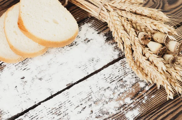 小麦とケシの1束と 古い素朴な木製の板に小麦粉とパンのスライスを散らした — ストック写真