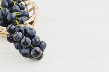 Taze olgun mavi üzüm eski ahşap rustik beyaz plakalar üzerinde hasır sepet dışarı dökülür