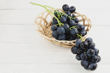 Taze olgun mavi üzüm eski ahşap rustik beyaz plakalar üzerinde hasır sepet dışarı dökülür